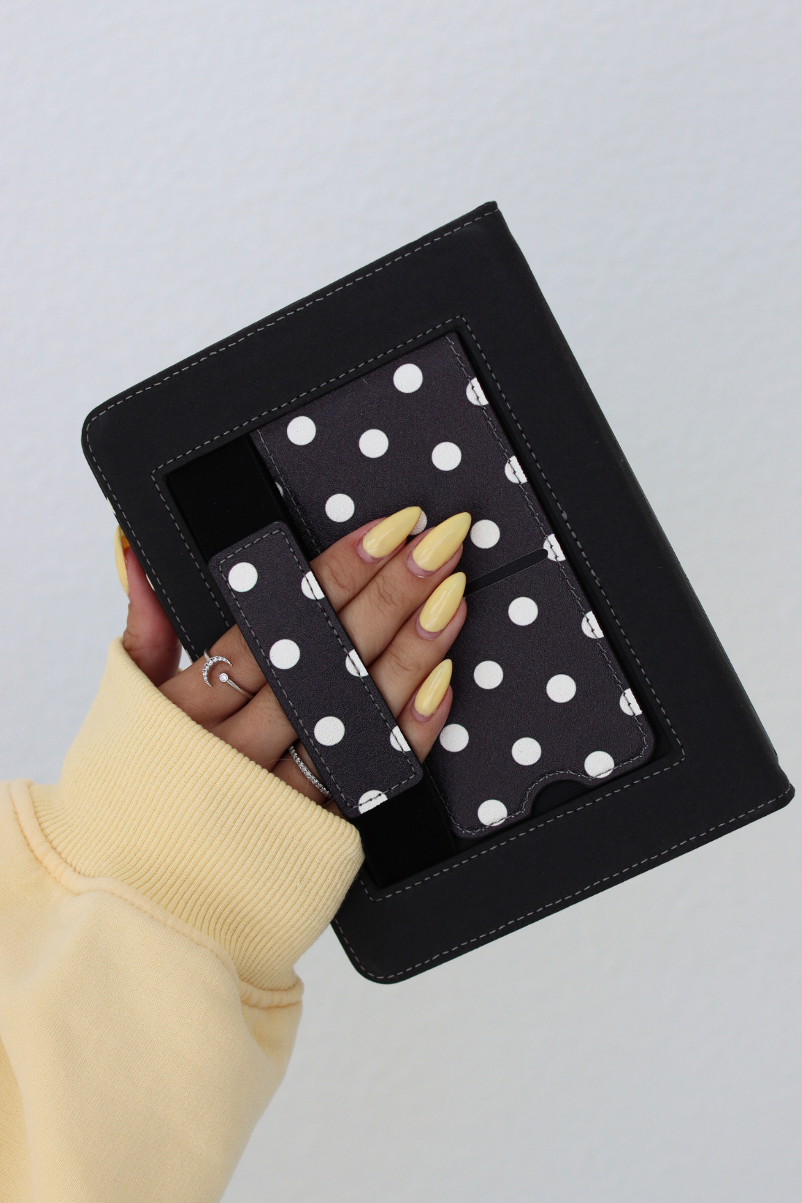 Hand holding a black kindle case with white polka dots against a light gray background