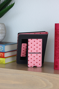 Pink polka dot case on a wooden surface with books and a plant in the background