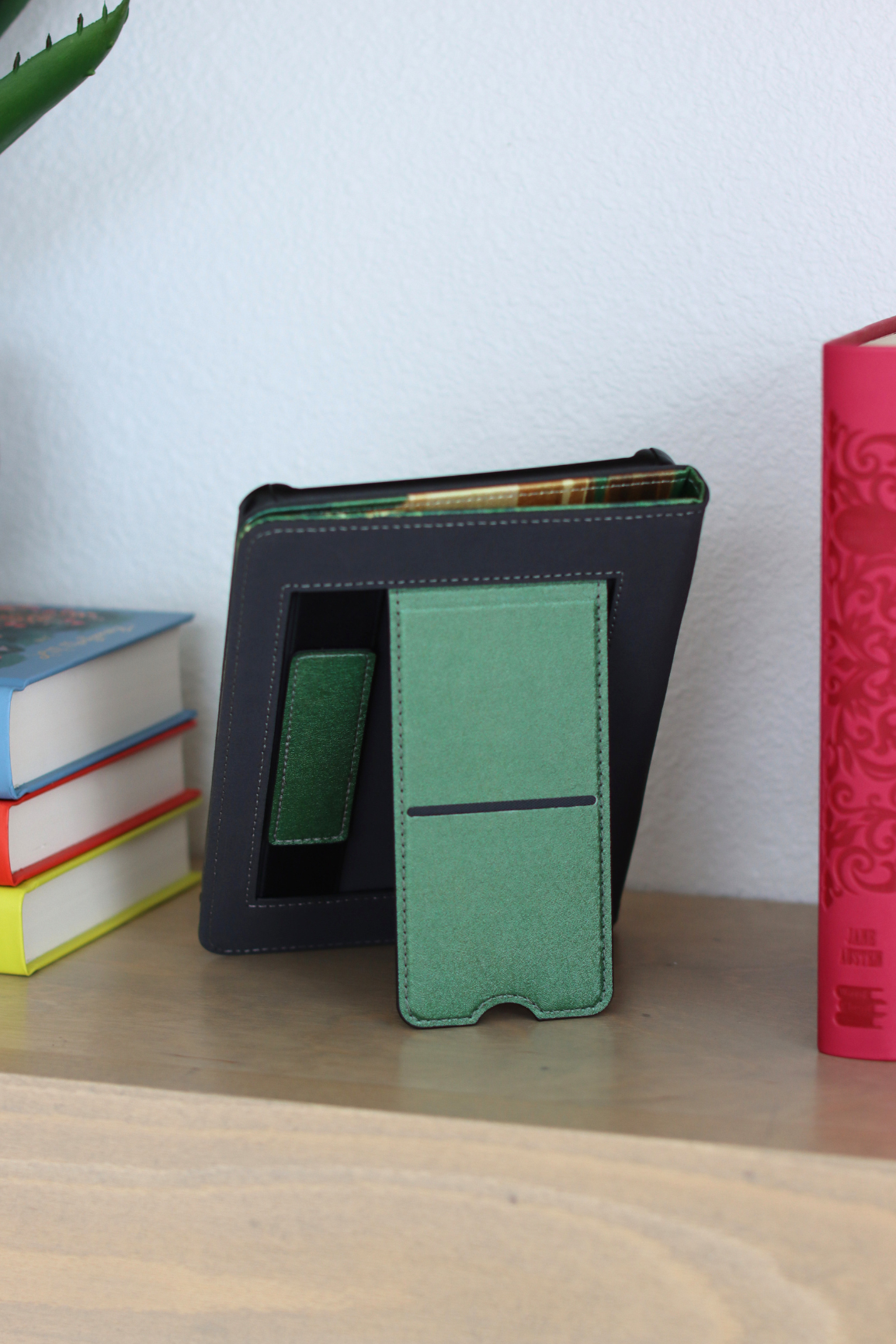 Green kindle on a wooden surface with books of different colors in the background.