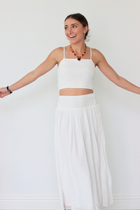 Woman wearing a white outfit with a necklace against a plain background