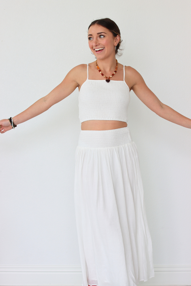 Woman wearing a white outfit with a necklace against a plain background