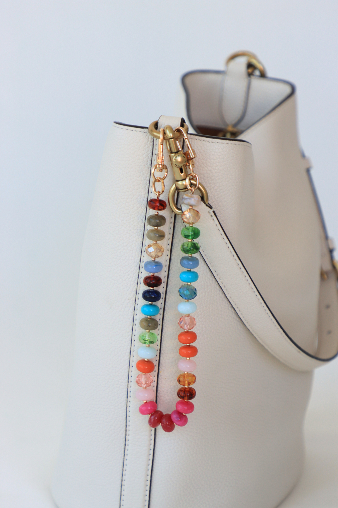 Colorful beaded handbag strap attached to a white handbag on a light gray background