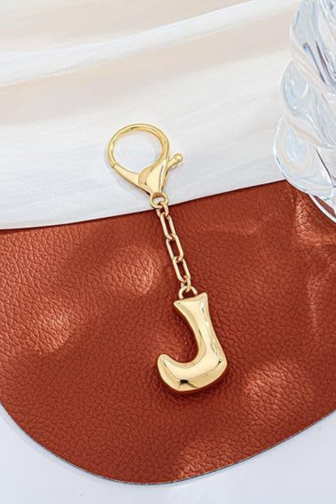 Gold keychain with letter 'J' on a brown leather surface