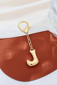 Gold keychain with letter 'J' on a brown leather surface