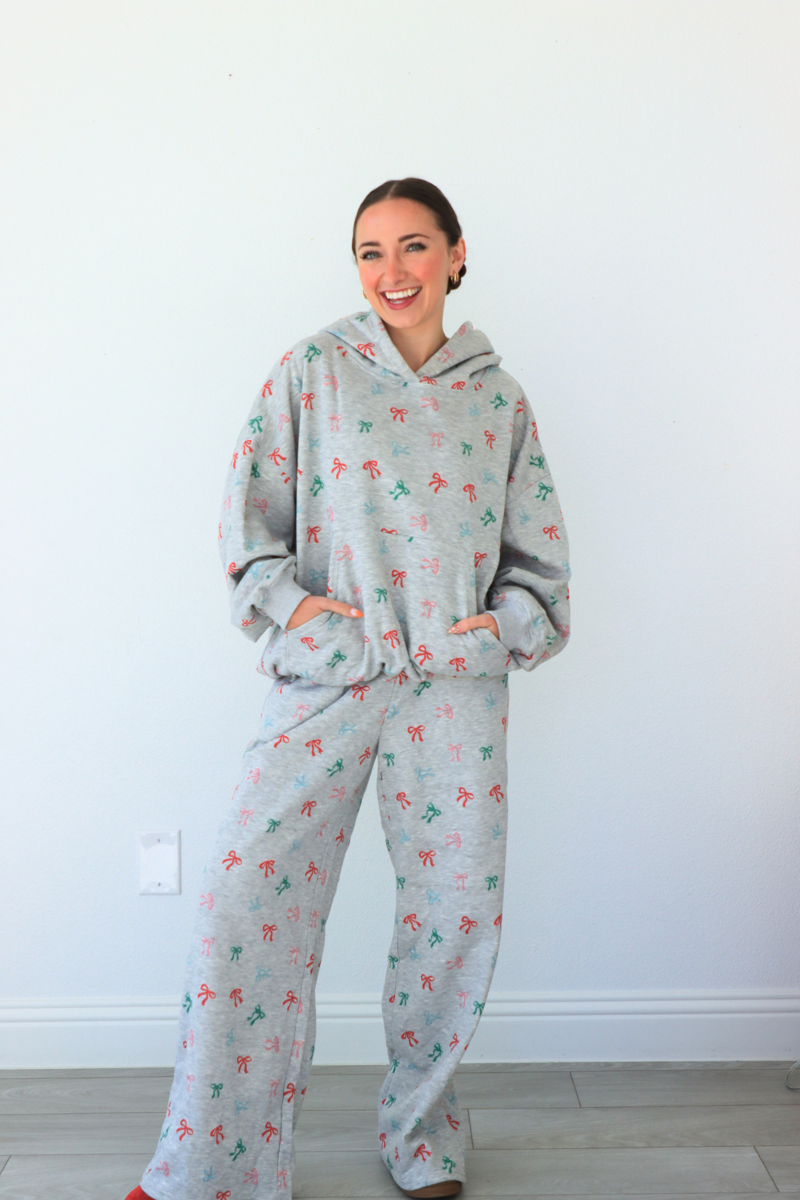 Woman wearing a gray hoodie and pants set with colorful patterns against a white wall.