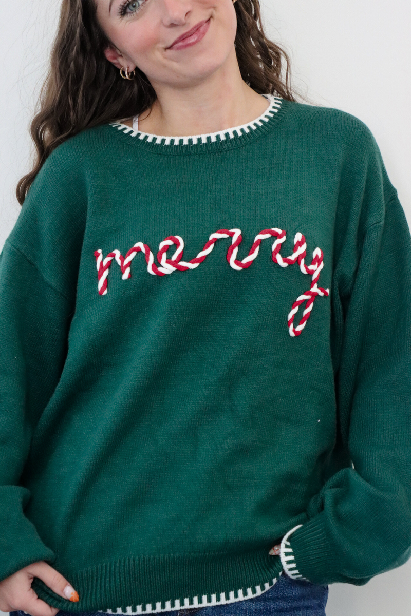 Person wearing a green sweater with 'merry' in red and white letters against a white background