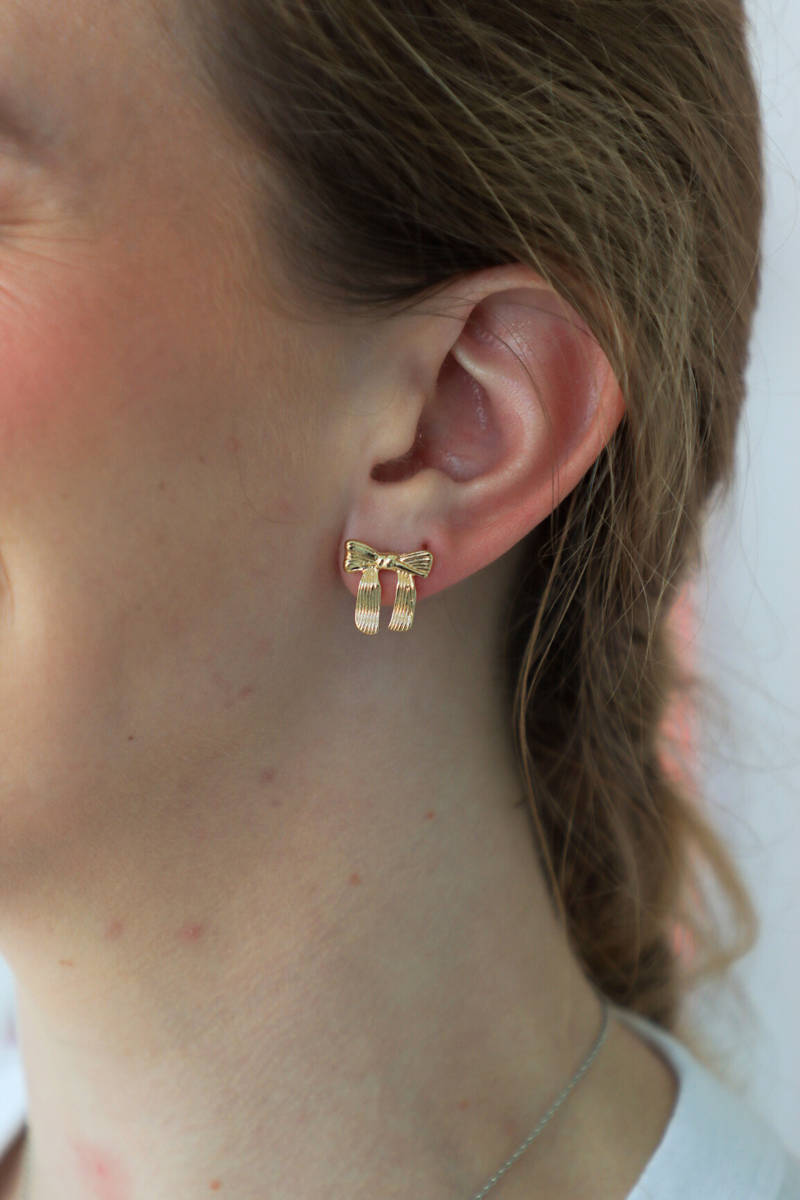 Gold bow-shaped earring worn by a person with a neutral background