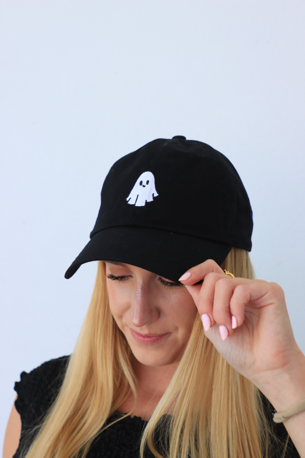 Person wearing a black cap with a white ghost logo against a light blue background