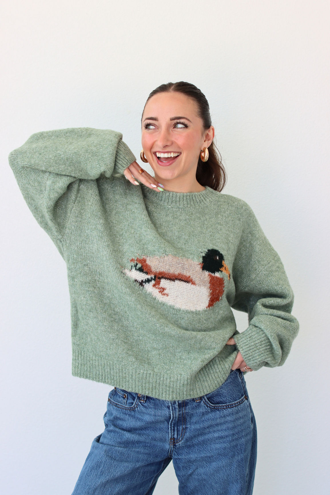 Woman wearing a green sweater with a duck design against a white background