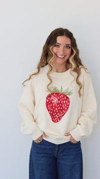 Woman wearing a cream sweater with a strawberry design against a white background
