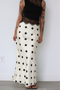 Person wearing a black top and white polka dot skirt against a plain background