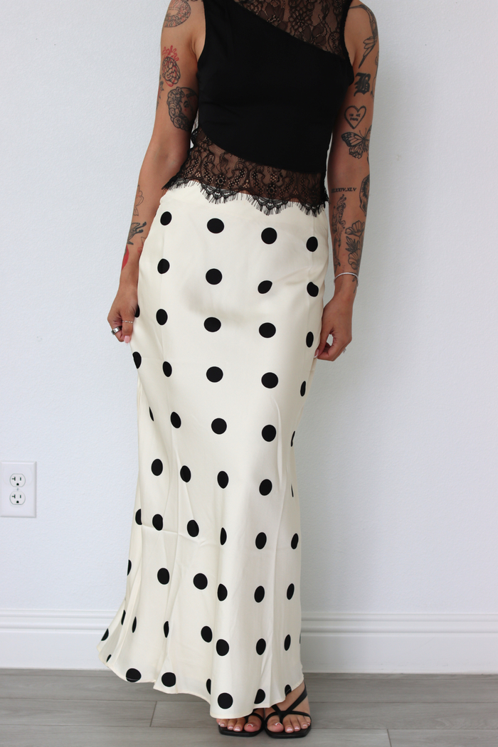 Person wearing a black top and white polka dot skirt against a plain background