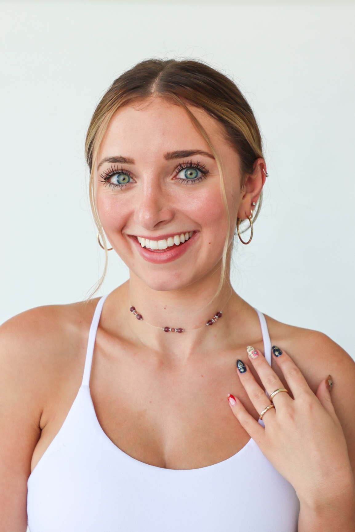 Woman wearing a necklace and showing a ring on her finger against a white background