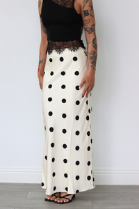 Person wearing a black top and white polka dot skirt against a plain background