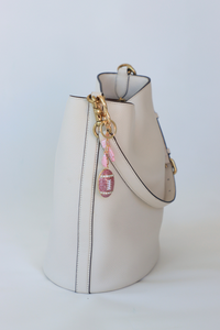 White bucket bag with gold chain and pink charm on a white background