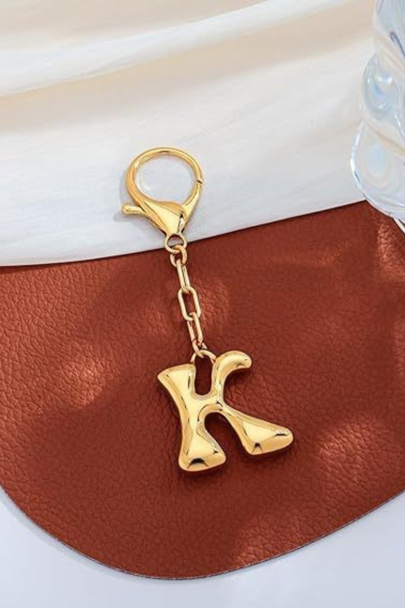 Gold keychain with letter 'K' on a brown leather surface