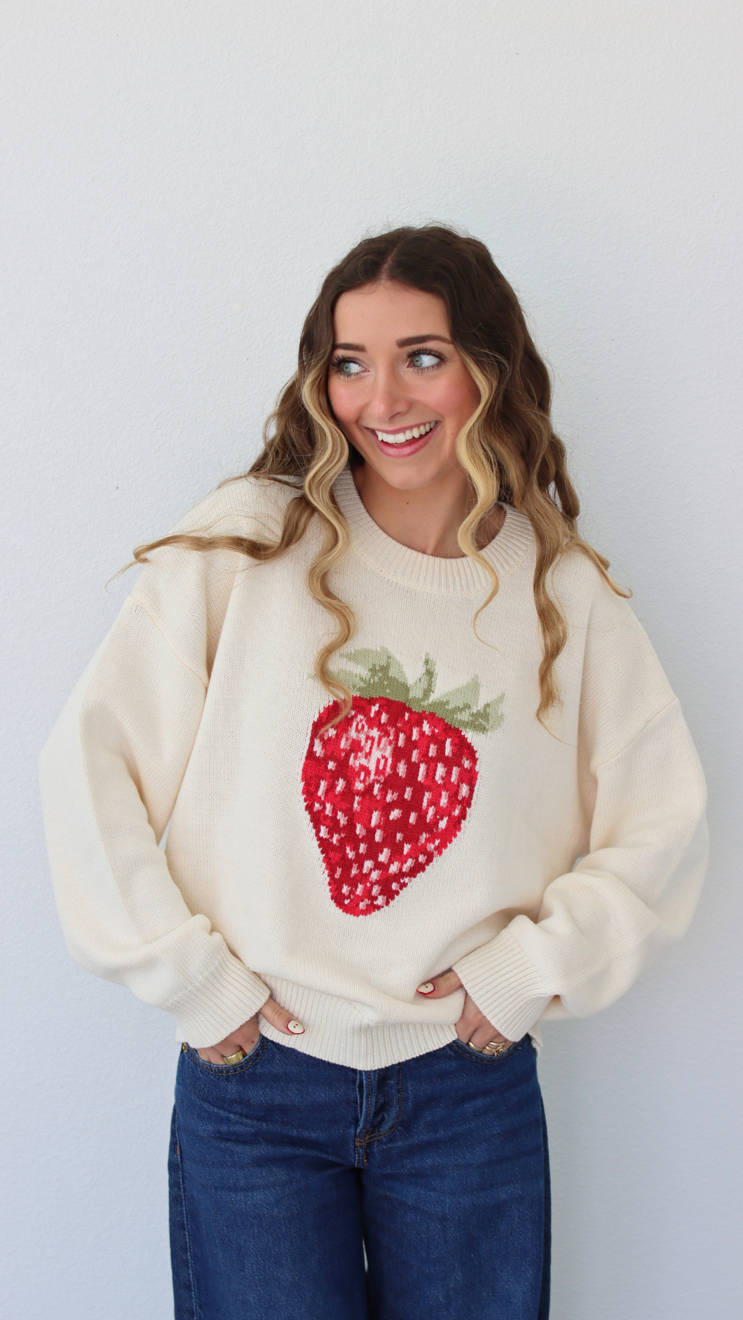 Woman wearing a cream sweater with a strawberry design against a white background
