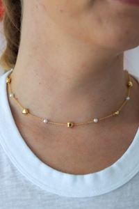 Gold necklace with heart-shaped pendants on a person wearing a white shirt.