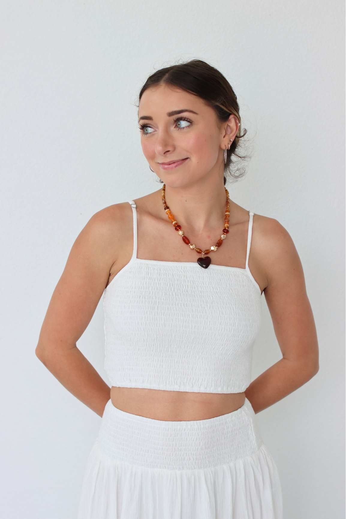 Woman wearing a white top and skirt with a necklace on a plain background