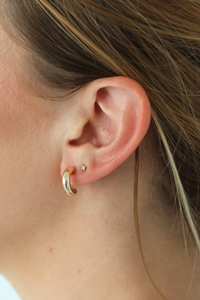 Close-up of an ear with gold hoop earrings.