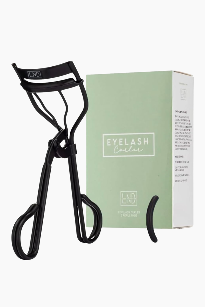 A black eyelash curler shown next to its mint green and white packaging box on a clean white background.