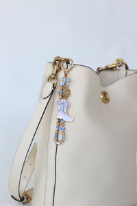 White handbag with decorative keychain on a light blue background