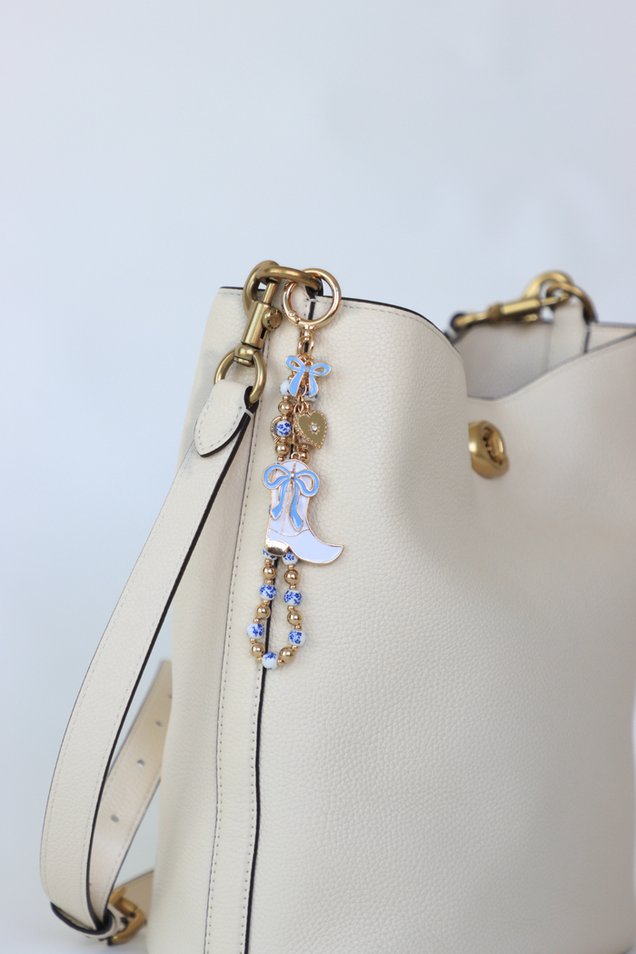 White handbag with decorative keychain on a light blue background