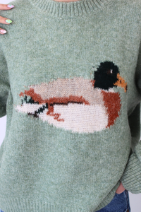 Green sweater with a knitted duck design on a plain background