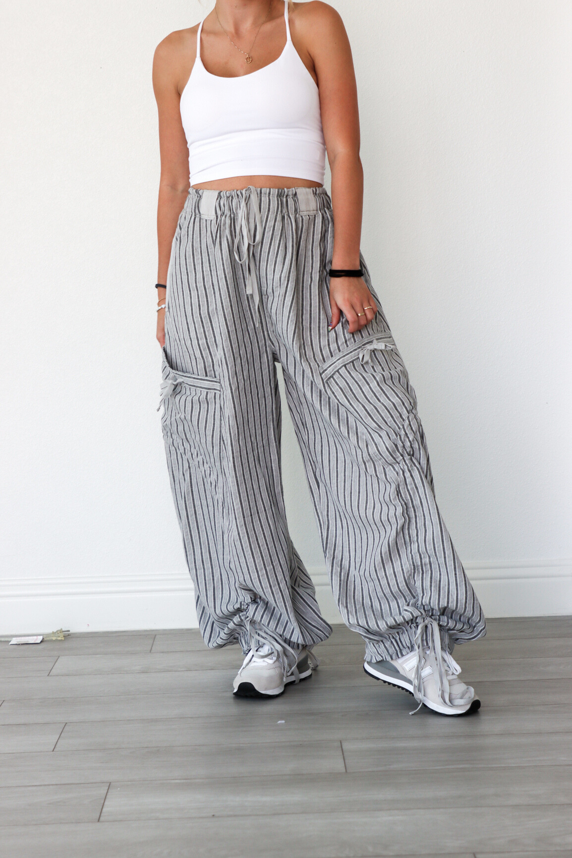 Person wearing a white crop top and gray striped wide-leg pants on a light wooden floor.