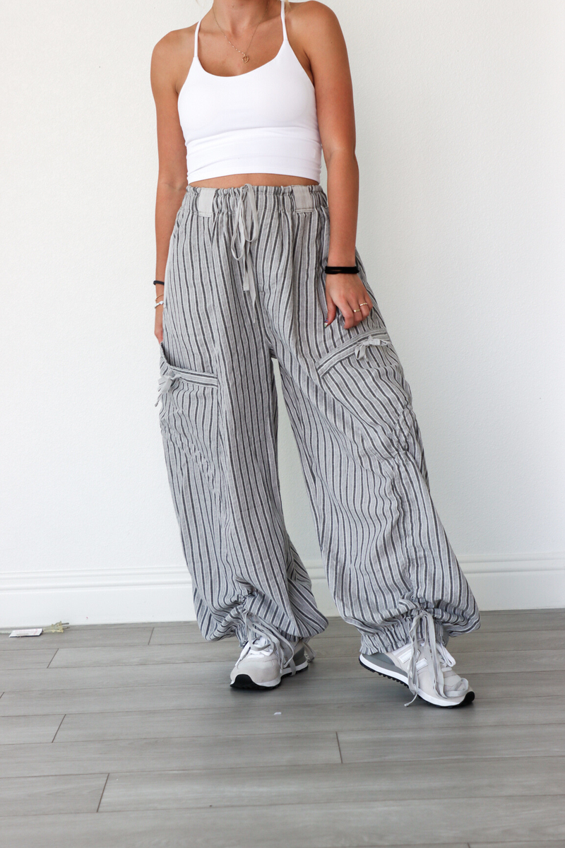 Person wearing a white crop top and gray striped wide-leg pants on a light wooden floor.