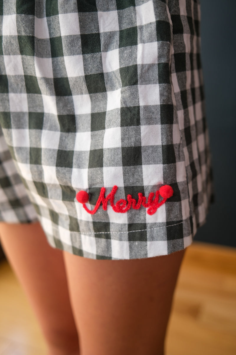 girl wearing plaid pajama shorts with "merry" embroidering