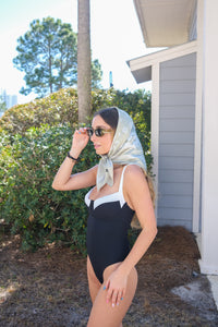 Woman in a black swimsuit with a white top, standing outdoors near a house.