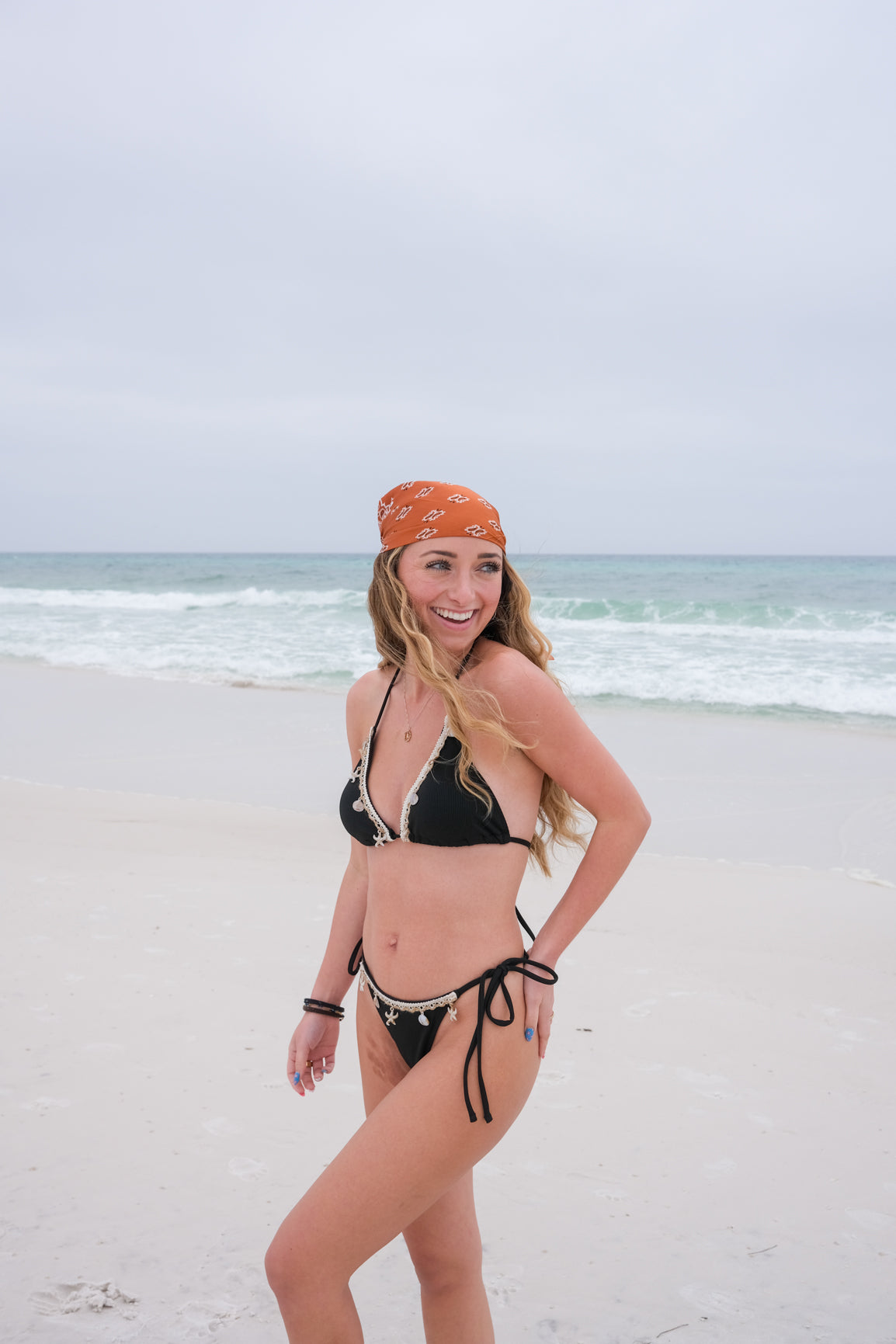 Woman in a black bikini and orange headband standing on a beach.