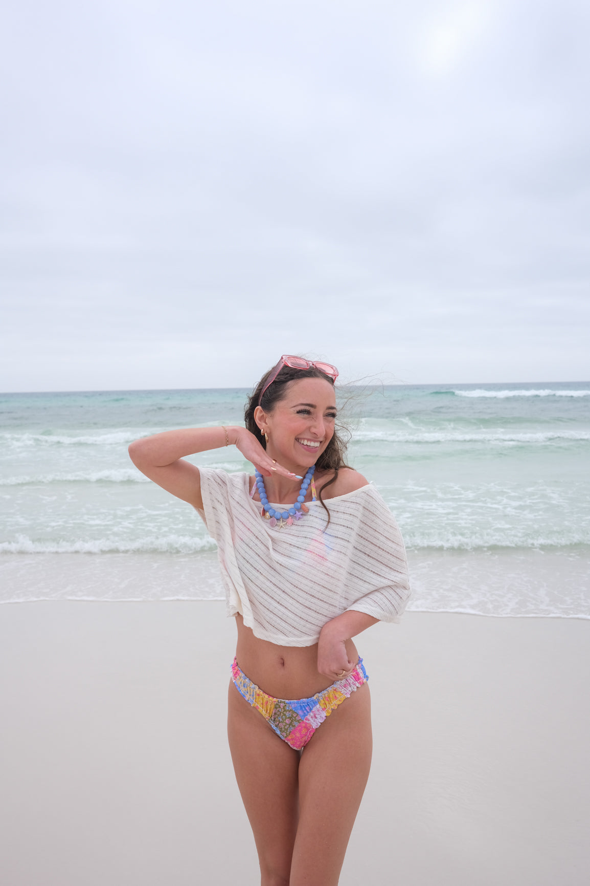 Woman in a colorful bikini and off-shoulder top standing on a beach with ocean in the background