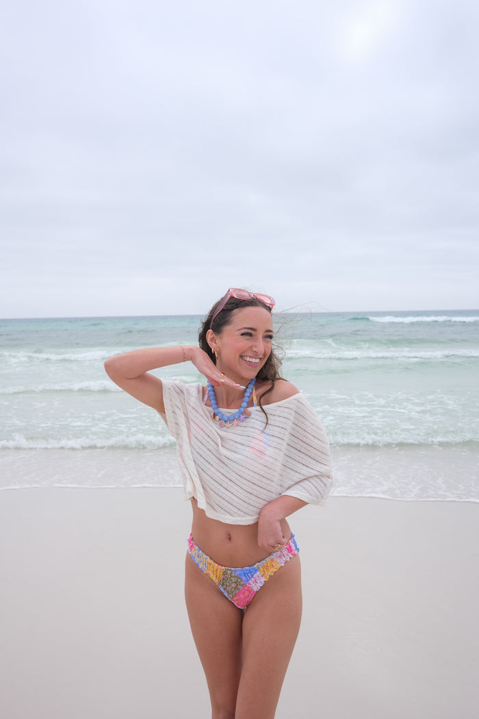 Woman in a colorful bikini and off-shoulder top standing on a beach with ocean in the background
