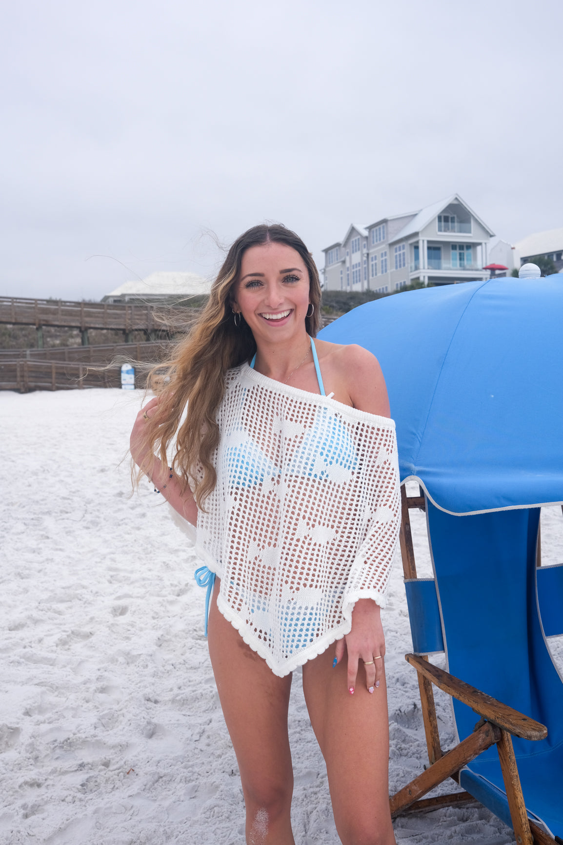 Woman on a beach with a blue umbrella and chair in the background