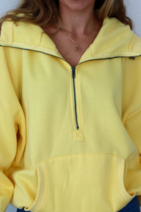 Yellow hoodie with a zipper worn by a person, against a plain background