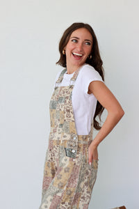 Woman wearing a patterned overall over a white shirt against a plain background