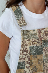 Patchwork overalls with patterns worn over a white t-shirt.