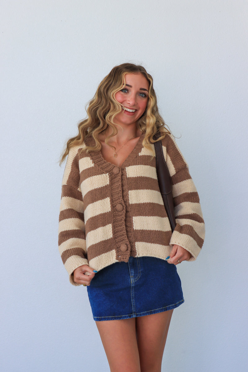 Woman wearing a brown and beige striped cardigan with a blue skirt against a light blue background