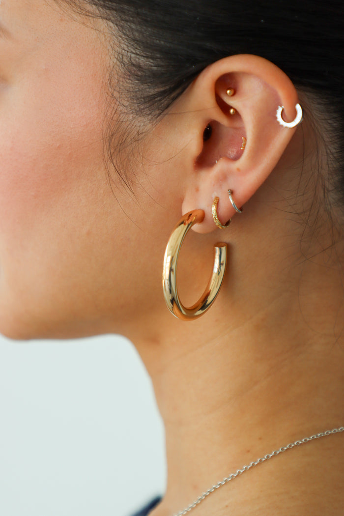 Close-up of an ear with gold hoop earrings and a blurred background