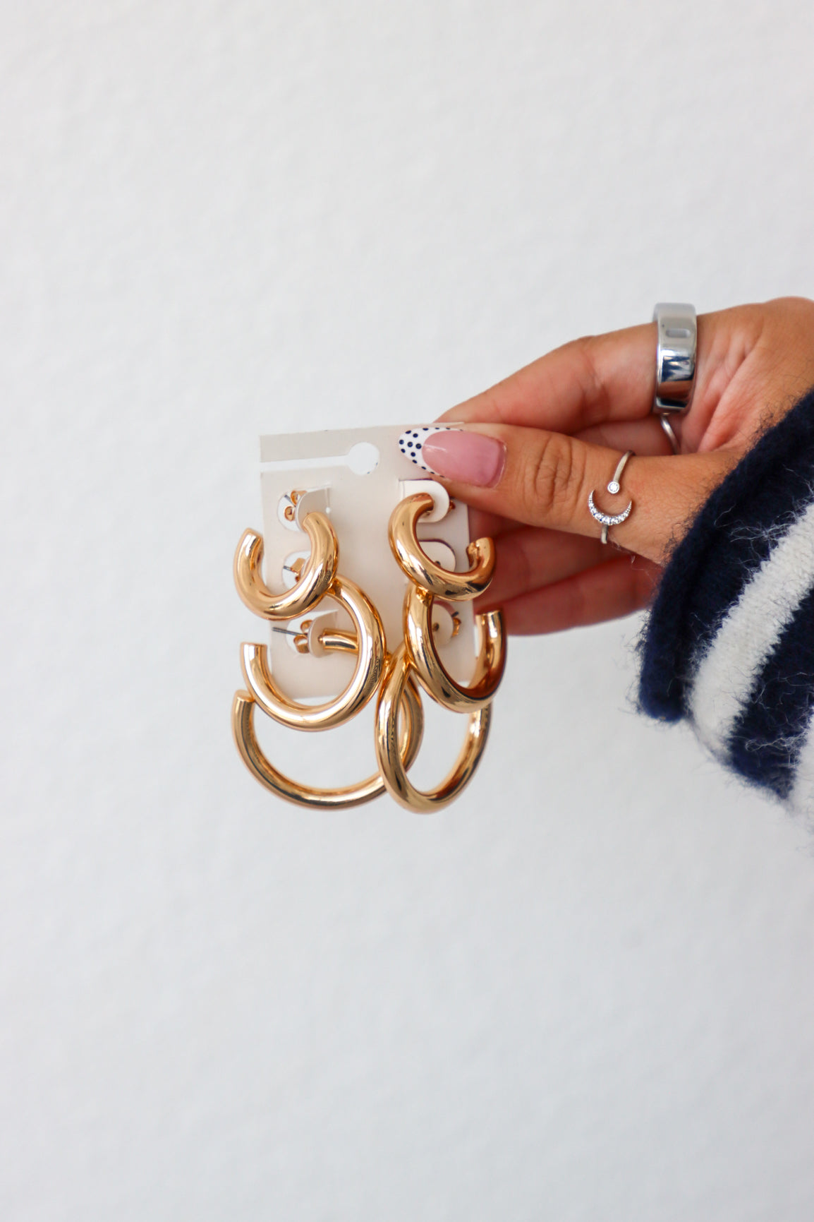 Hand holding a pack of gold hoop earrings against a white background