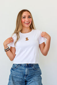 Woman wearing a white t-shirt with a small logo, smiling against a plain background