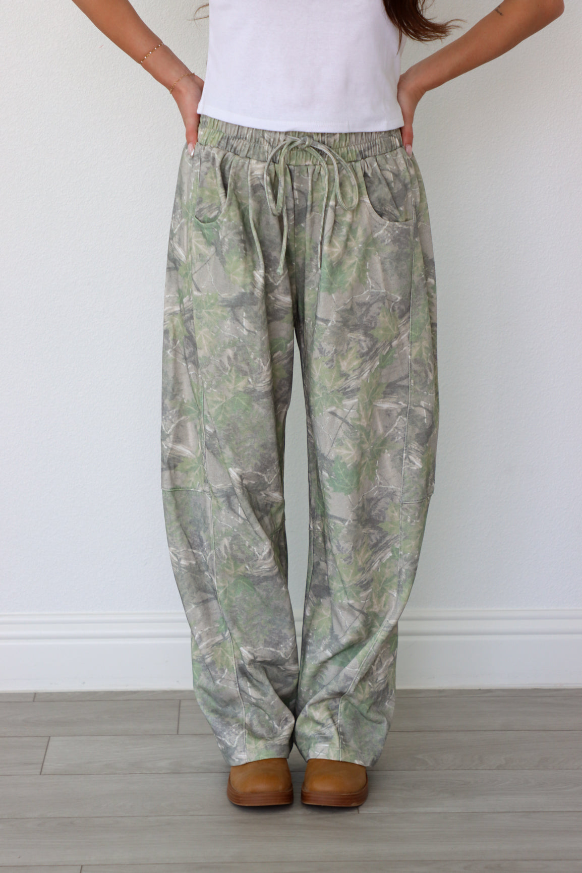 Person wearing camouflage pants and white shirt against a plain background