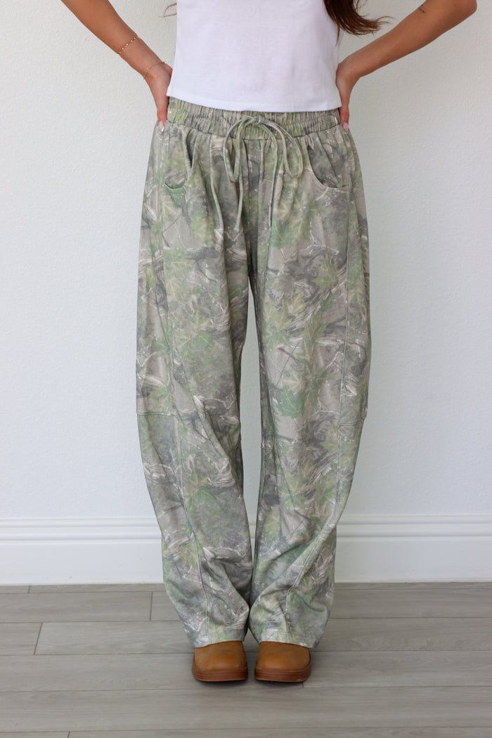 Person wearing camouflage pants and white shirt against a plain background