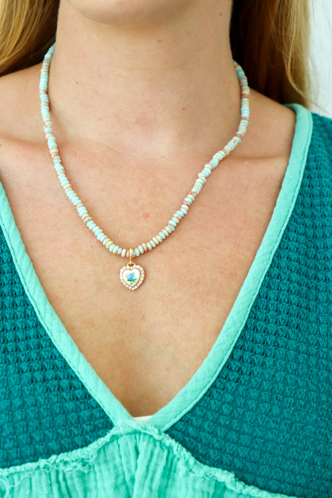 Person wearing a turquoise beaded necklace with a heart pendant, against a blurred background.