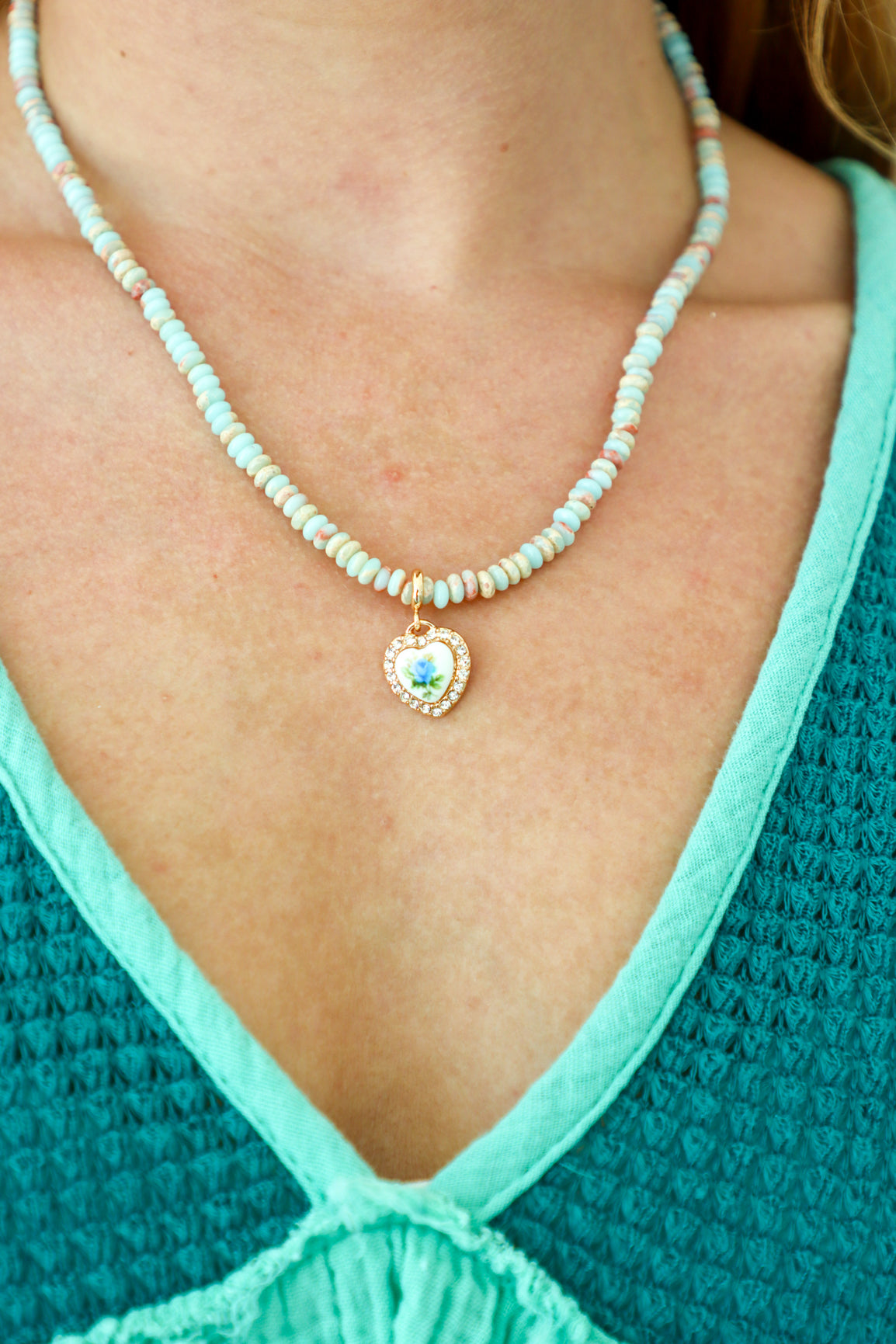 Necklace with a heart-shaped pendant worn by a person in a teal top