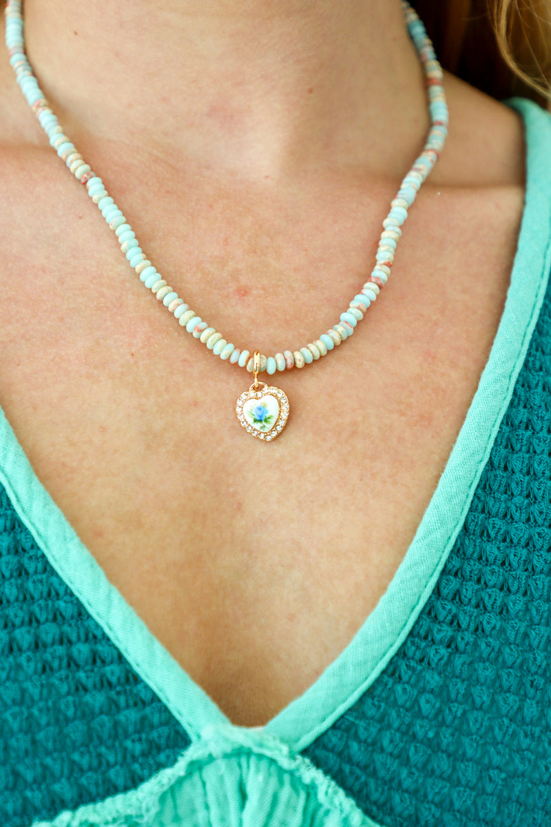 Necklace with a heart-shaped pendant worn by a person in a teal top