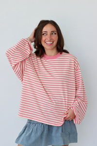 Woman wearing a pink and white striped shirt with a light blue skirt against a plain background