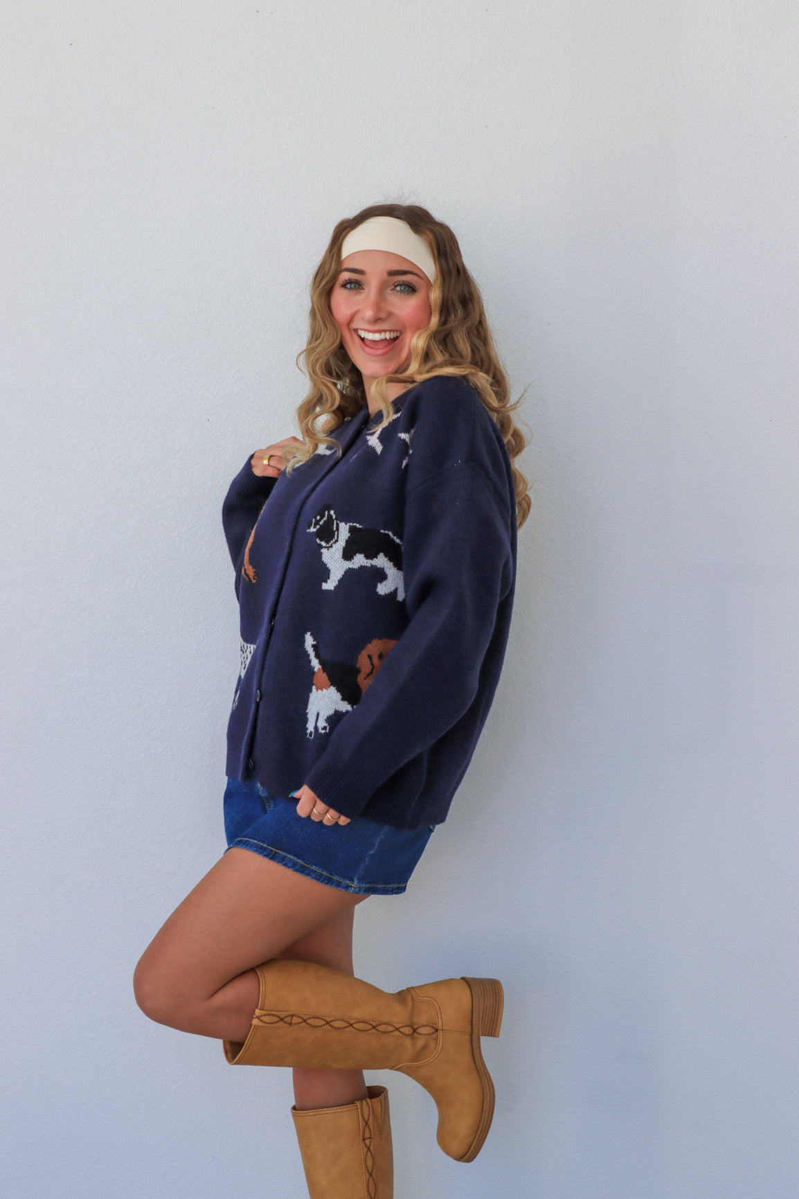 Woman wearing a navy sweater with cat prints, a blue skirt, and tan boots against a light gray background